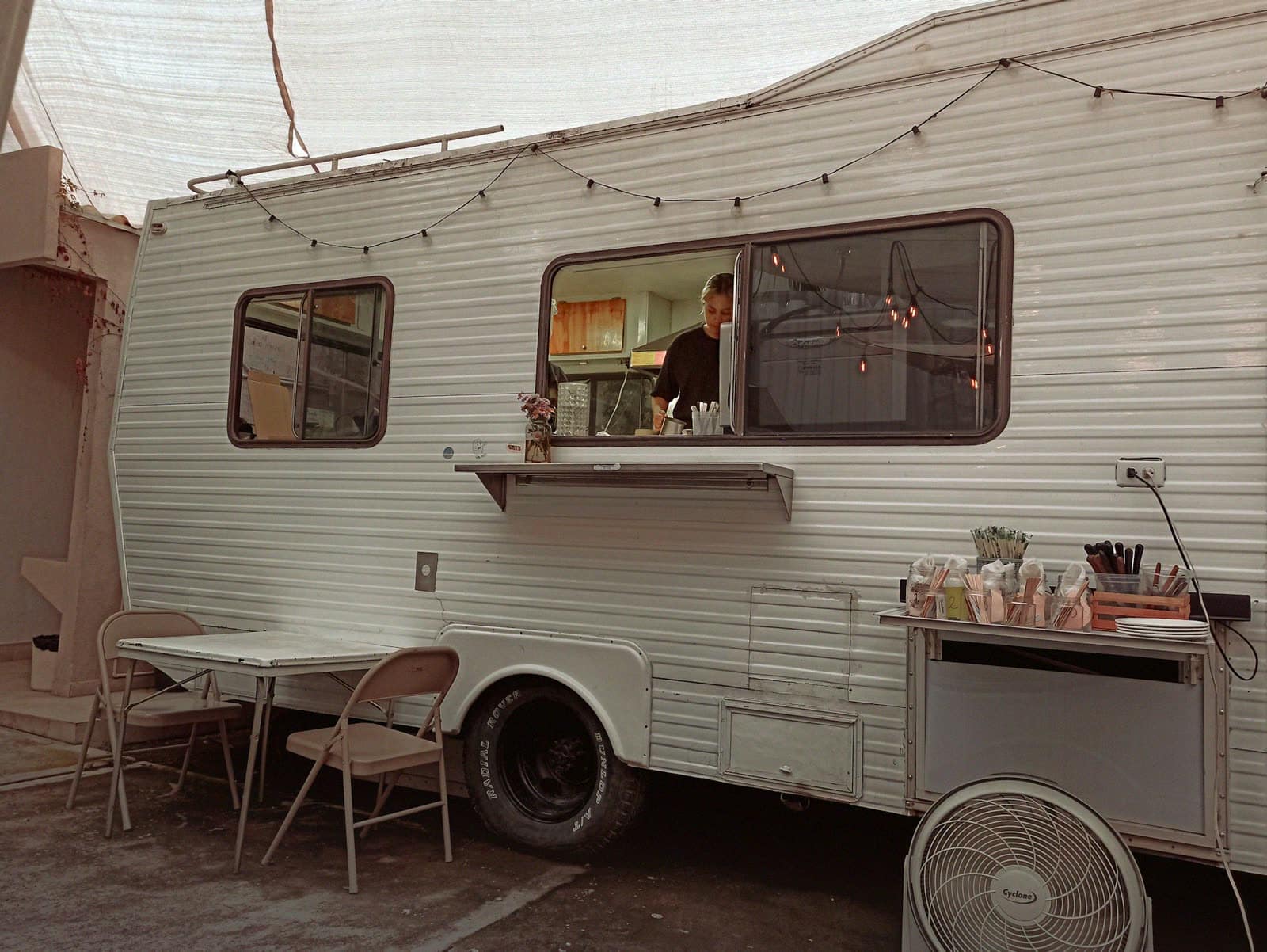 A vintage trailer with its service window open and string lights
