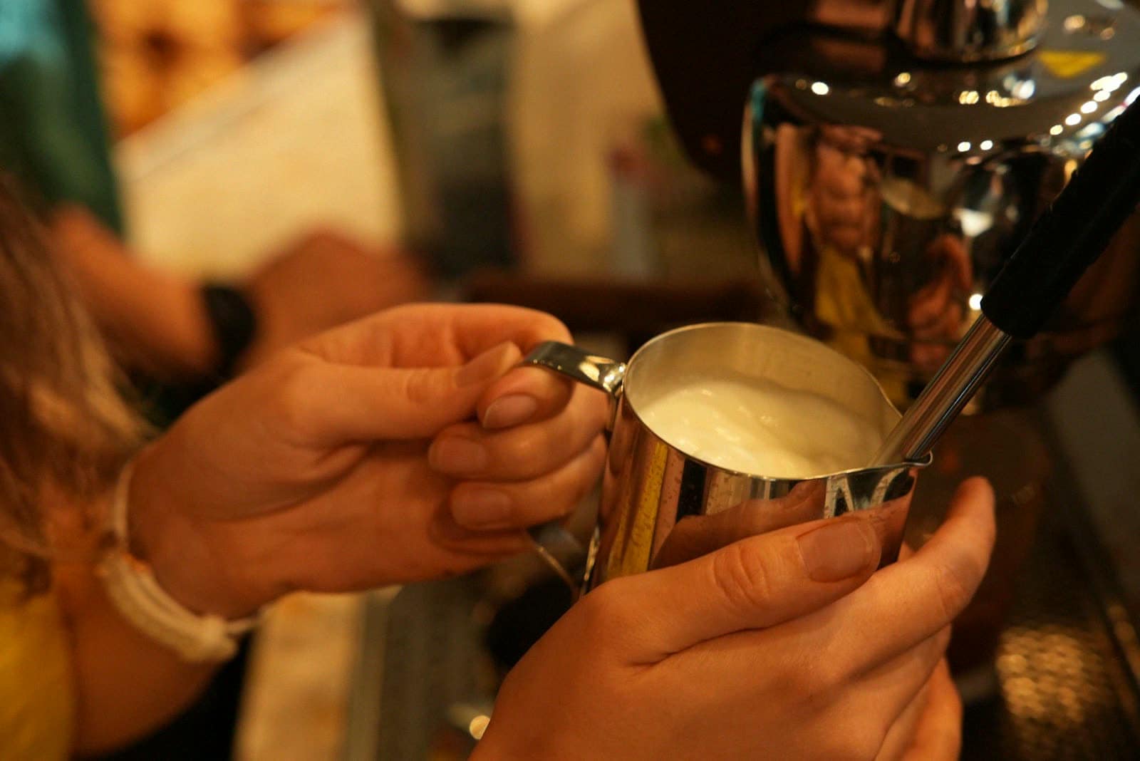 Hands steaming milk in a pitcher at an espresso machine