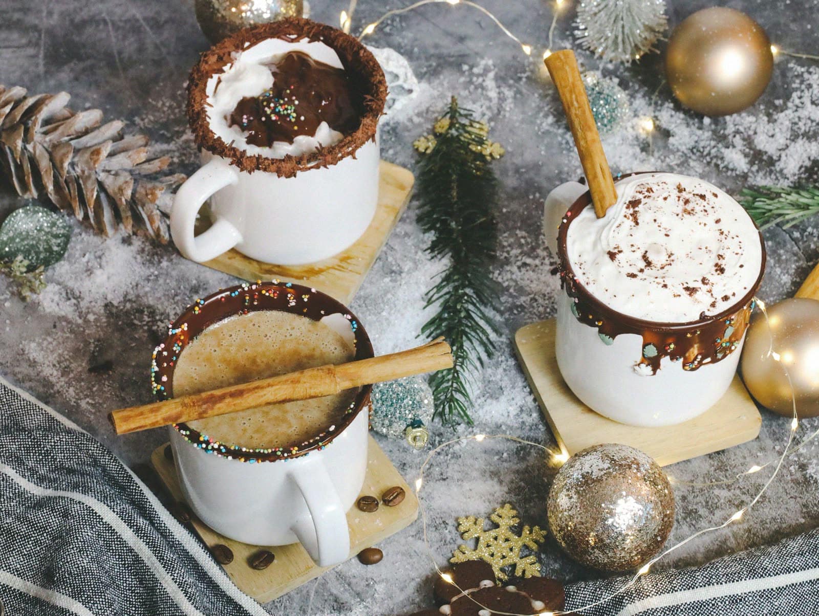 Mugs of hot chocolate and coffee with cinnamon sticks among holiday decorations