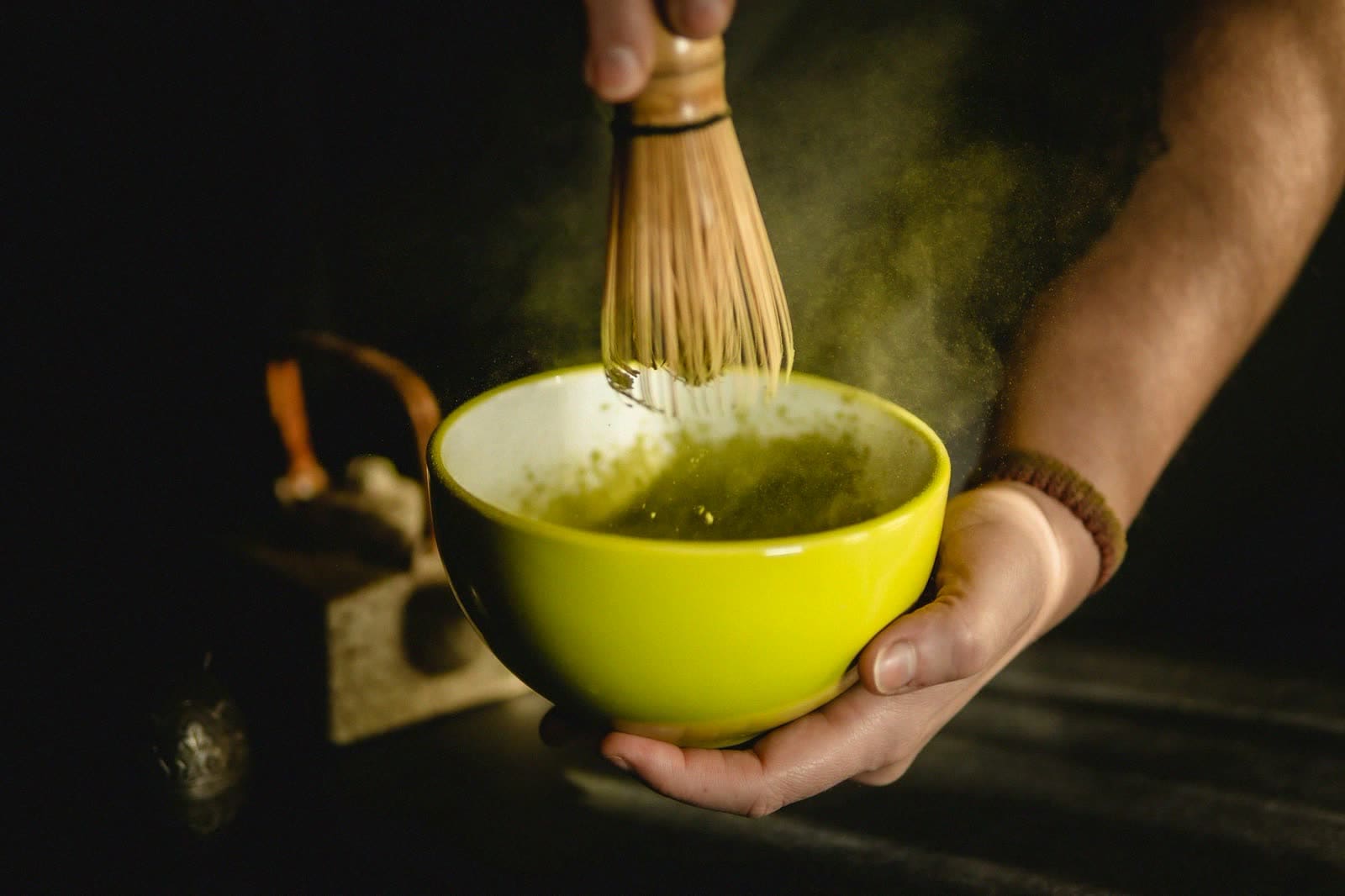 Hands whisking matcha in a yellow bowl with a bamboo whisk