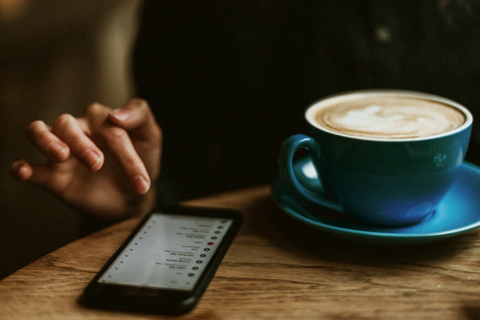 A phone on a cafe table beside a latte in a blue cup